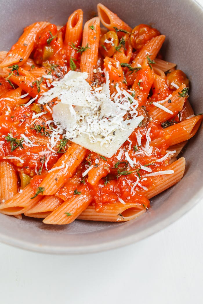 Close-up of penne pasta in rich tomato sauce topped with cheese, perfect for an Italian meal.